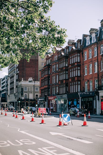 An aerial view of a busy residential street in Mayfair showing a row of parked cars along the curb, with some vehicles actively moving through an intersection. The street is lined with a mix of histor